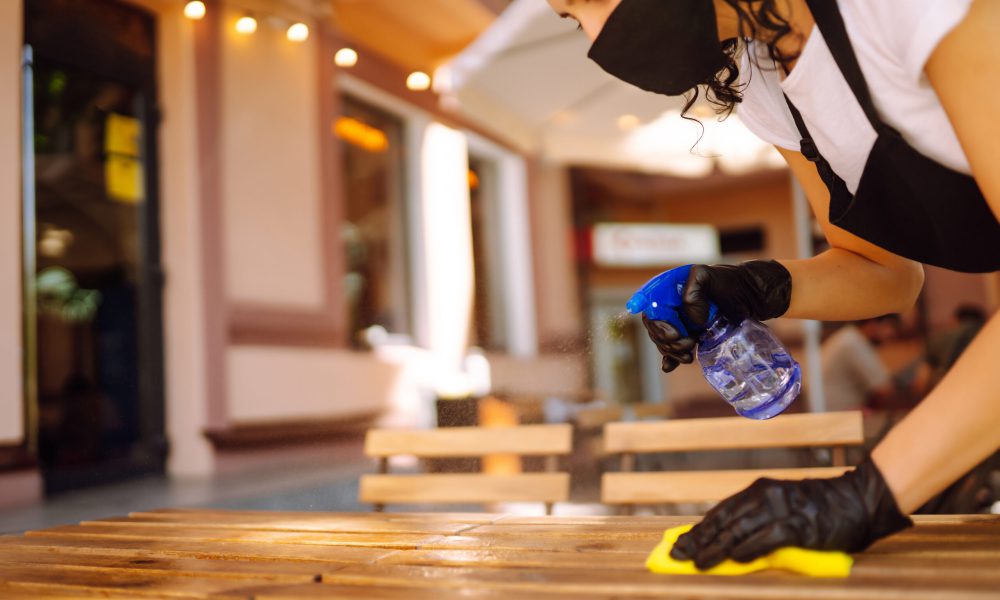 Disinfecting to prevent COVID-19. Young waitress cleaning table with disinfectant spray.