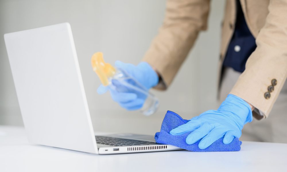 Close up of businessman hand wear glove using microfiber cloth and alcohol sanitizer spray to clean laptop in office.Disinfection ,cleanliness and heathcare,Anti Corona virus (COVID-19).