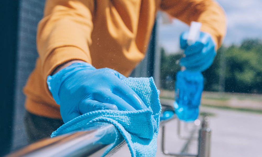 A young man disinfects a railing with a blue antiseptic and a rag in his hand. Protection and prevention from COVID-19