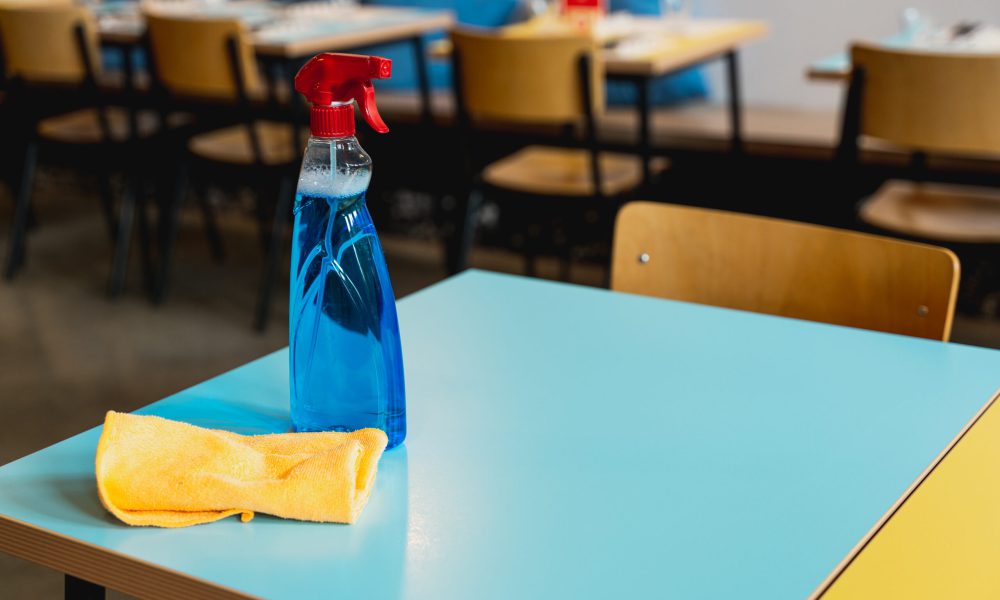 Close-up sanitizing spray diffuser detergent and cleaning cloth on restaurant table.