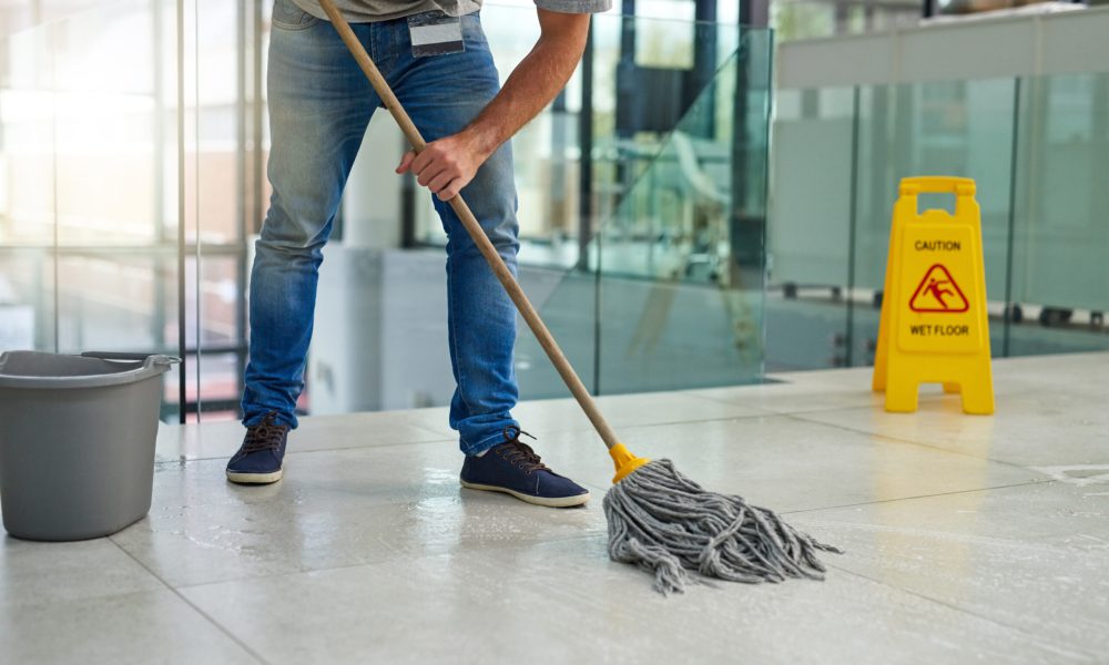 Shot of an unrecognizable man mopping the office floor.